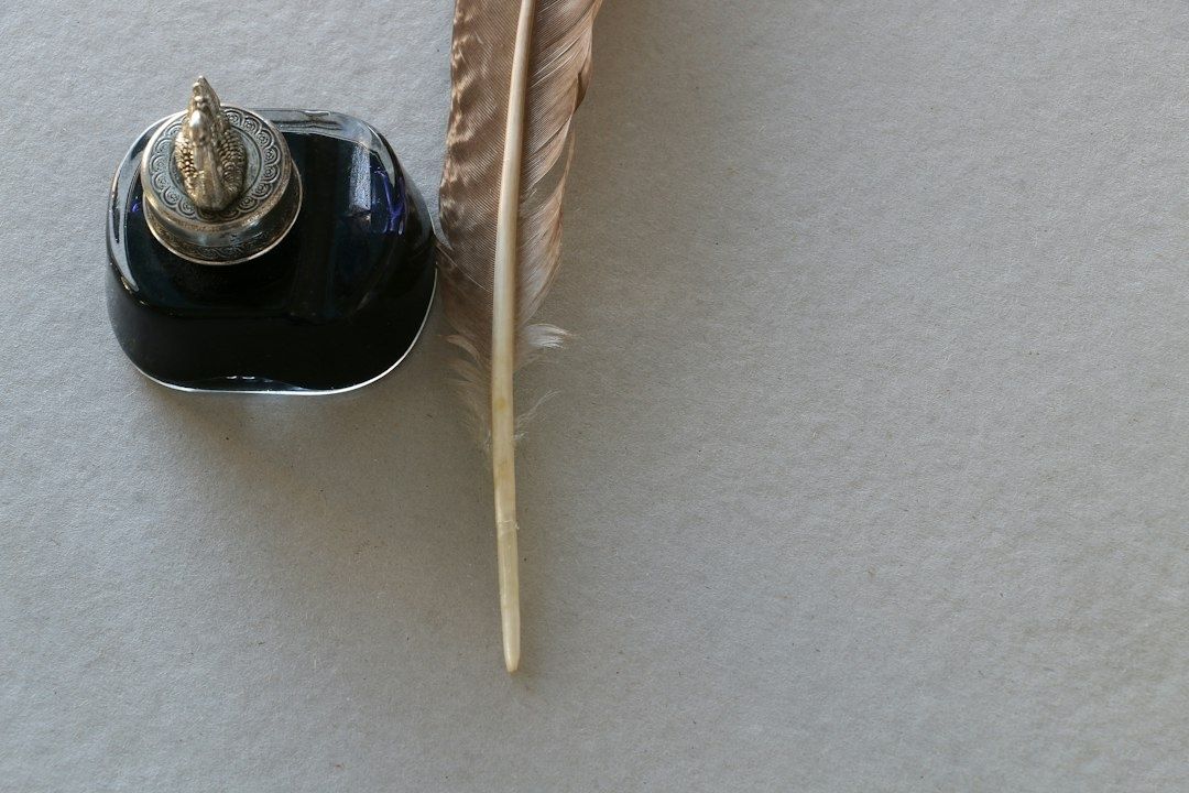 Schwarzes Tintenfass mit Feder auf hellem Papieruntergrund